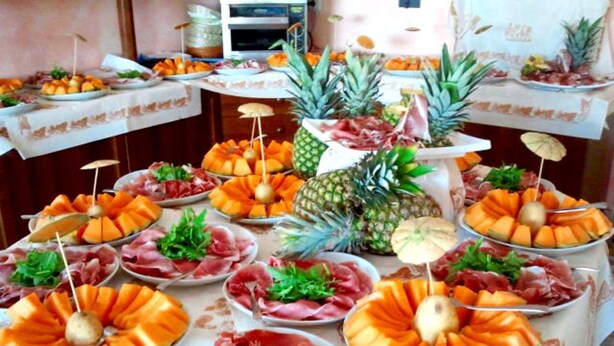 A buffet table with various food items including melon, pineapple, and prosciutto. - Hotel Etna (Riccione)