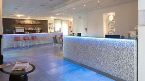 A reception area with a patterned reception desk, a bar area with chairs, and a wall clock. - Hotel Etna (Riccione)