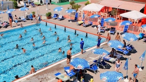 A swimming pool area with multiple pools, lounge chairs, umbrellas, and a water slide. - Hotel Etna (Riccione)