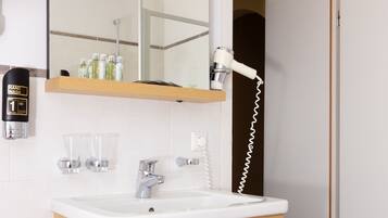 Baño con lavamanos blanco, tocador de madera, espejo, secamanos y toallero.