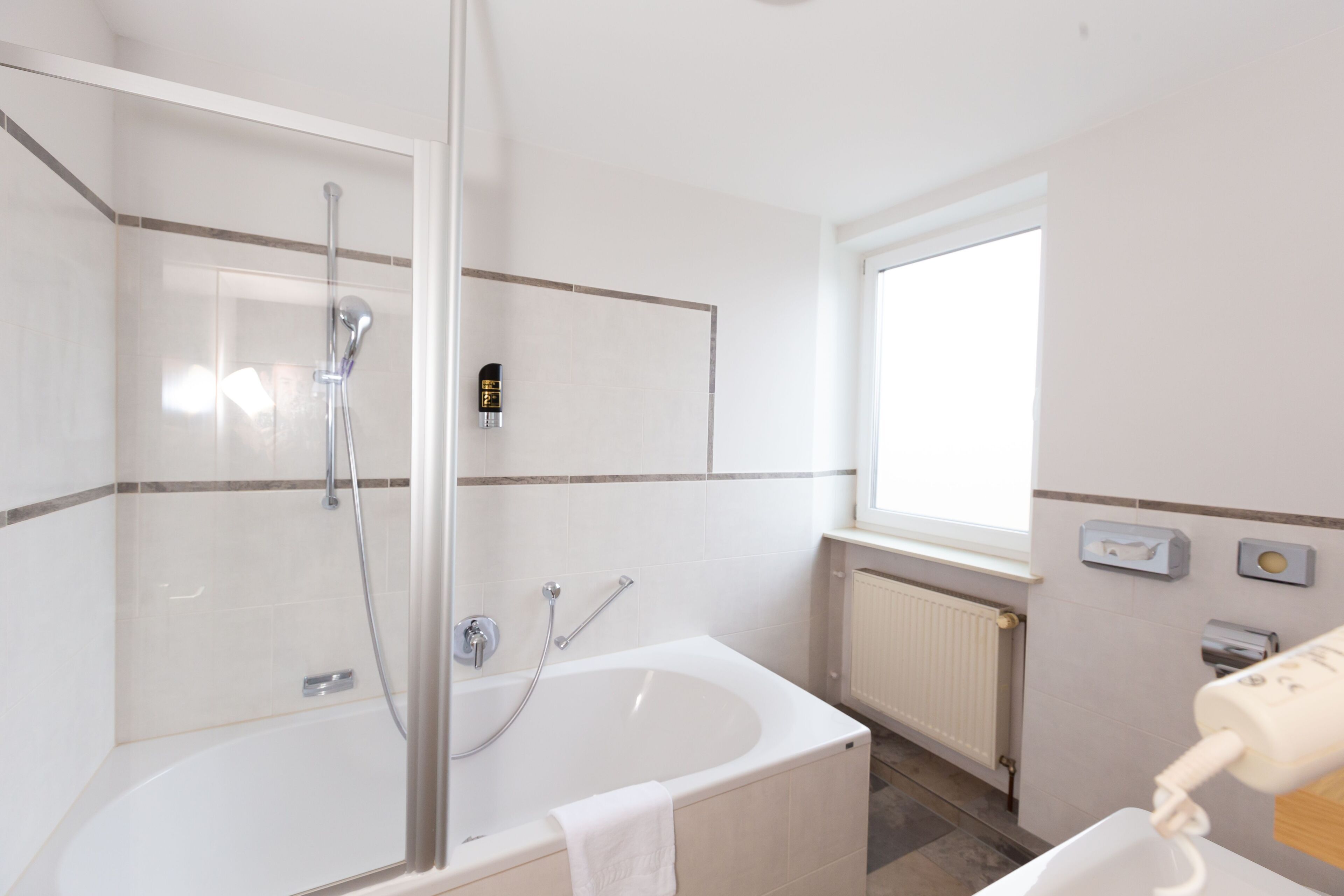 A modern bathroom with a glass-enclosed shower, a standalone bathtub, and a window providing natural light.