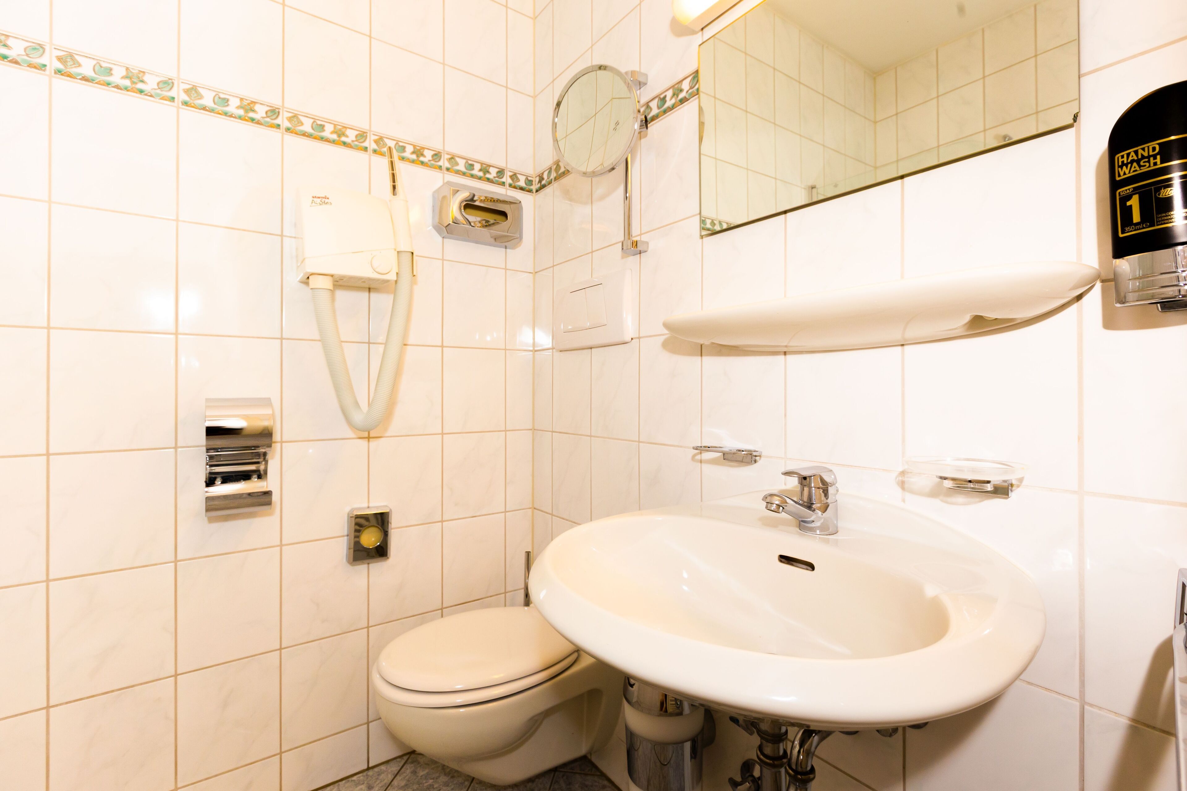 A bathroom with a toilet, sink, hand dryer, and a mirror.