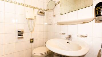 A bathroom with a toilet, sink, hand dryer, and a mirror.