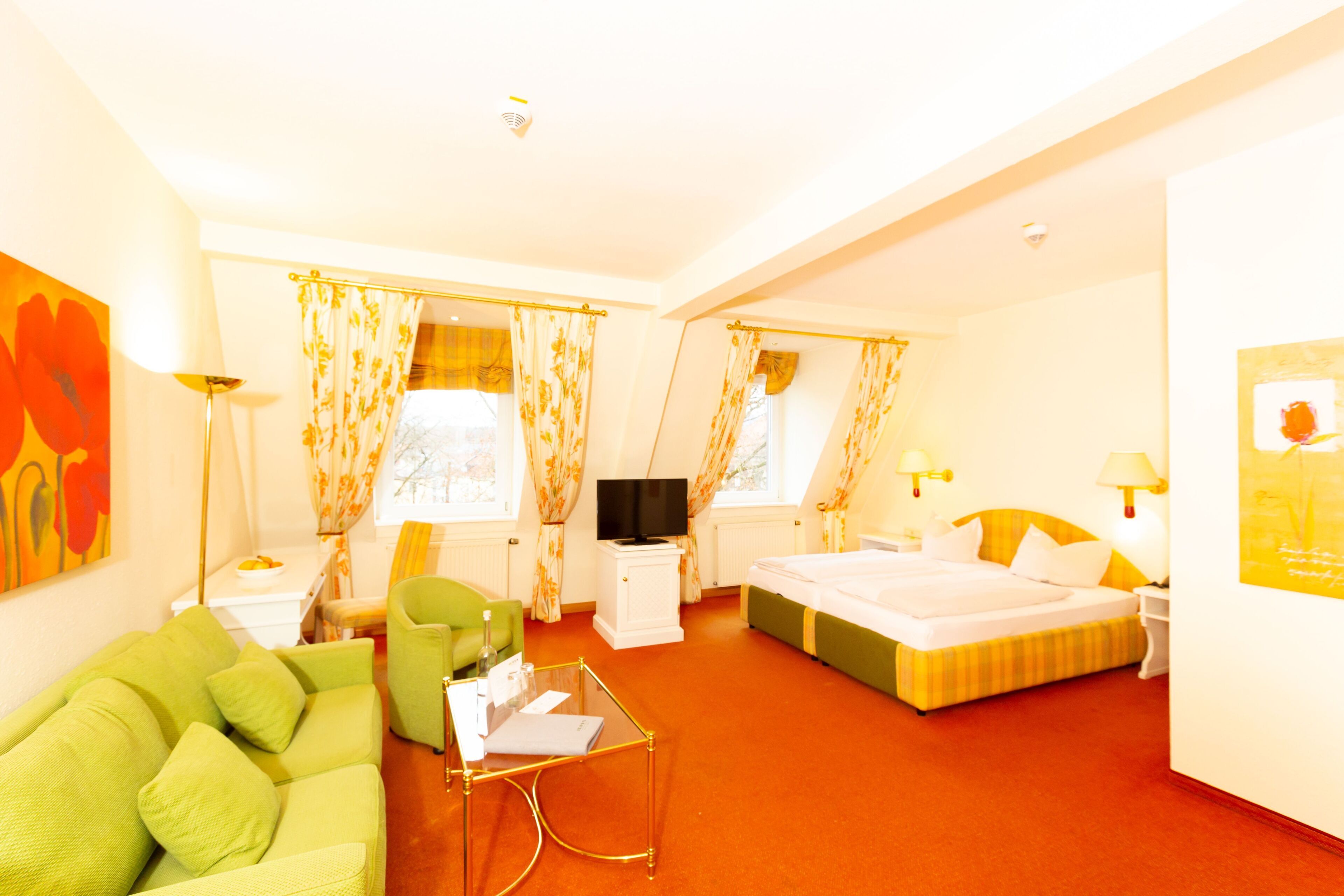Een hotelkamer met een groene bank, een bed, een televisie en een bureau met lamp.