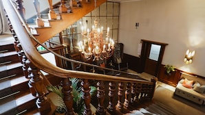 A grand staircase with a chandelier, wooden railings, and a seating area with a sign.
