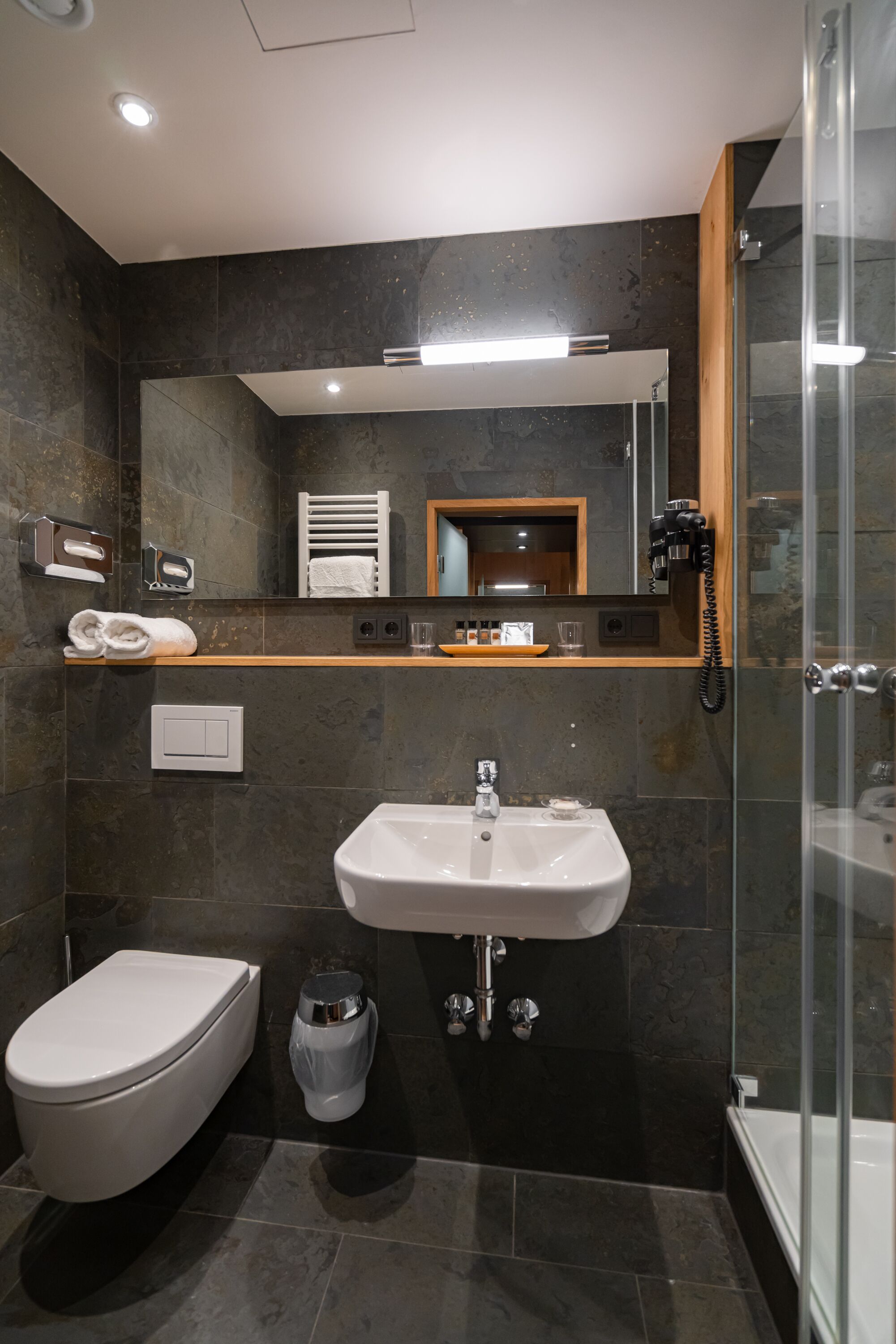 Un bagno moderno con un lavandino bianco, un water, un box doccia in vetro e uno specchio sopra il lavandino.