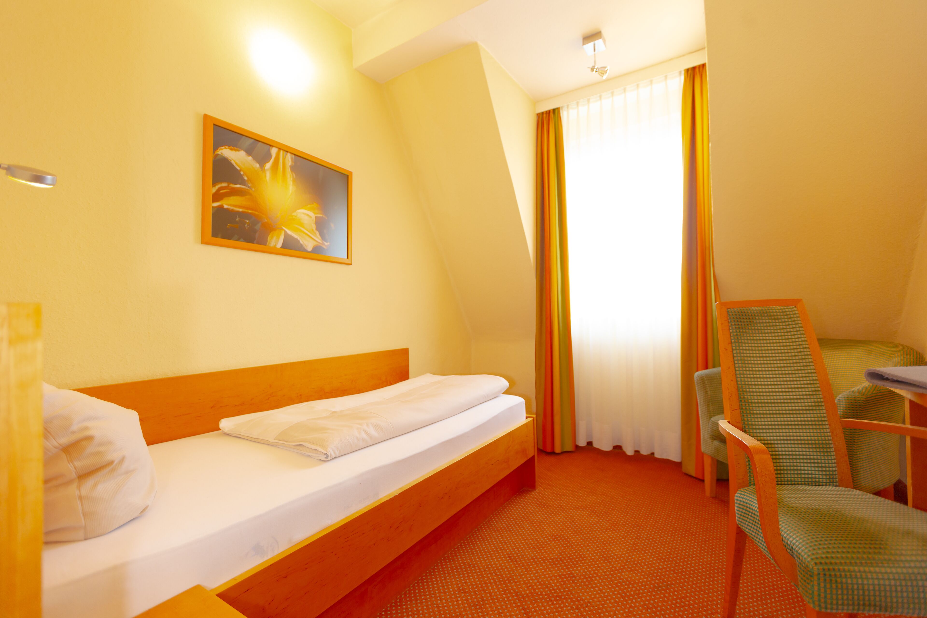 Une chambre d’hôtel avec un lit simple, une chaise, un bureau et un tableau au mur.
