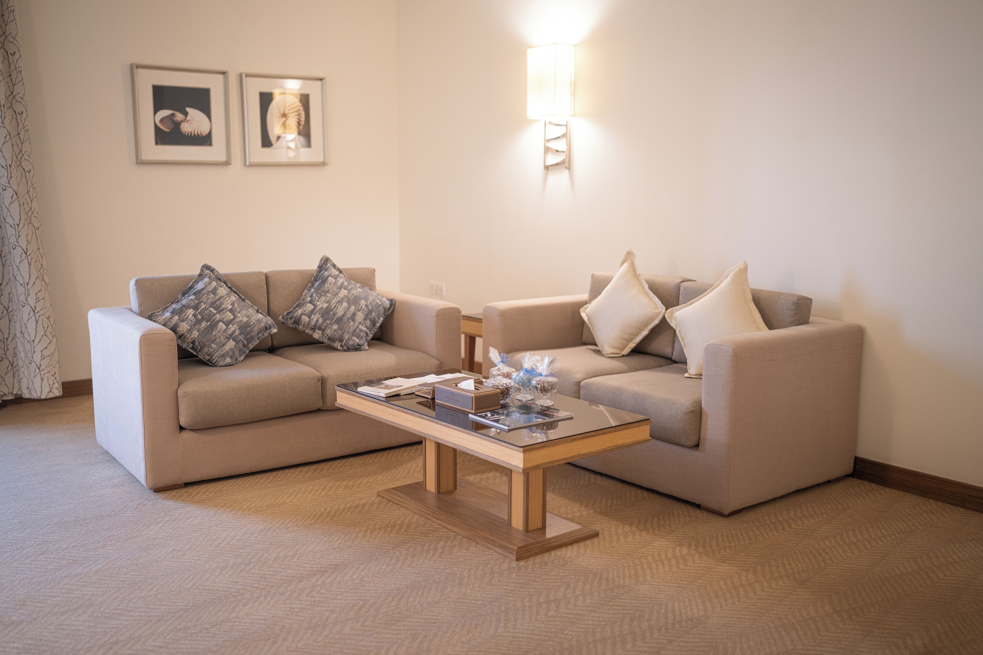 En stue med to beige sofaer, et glasbord og en vægmonteret lampe.