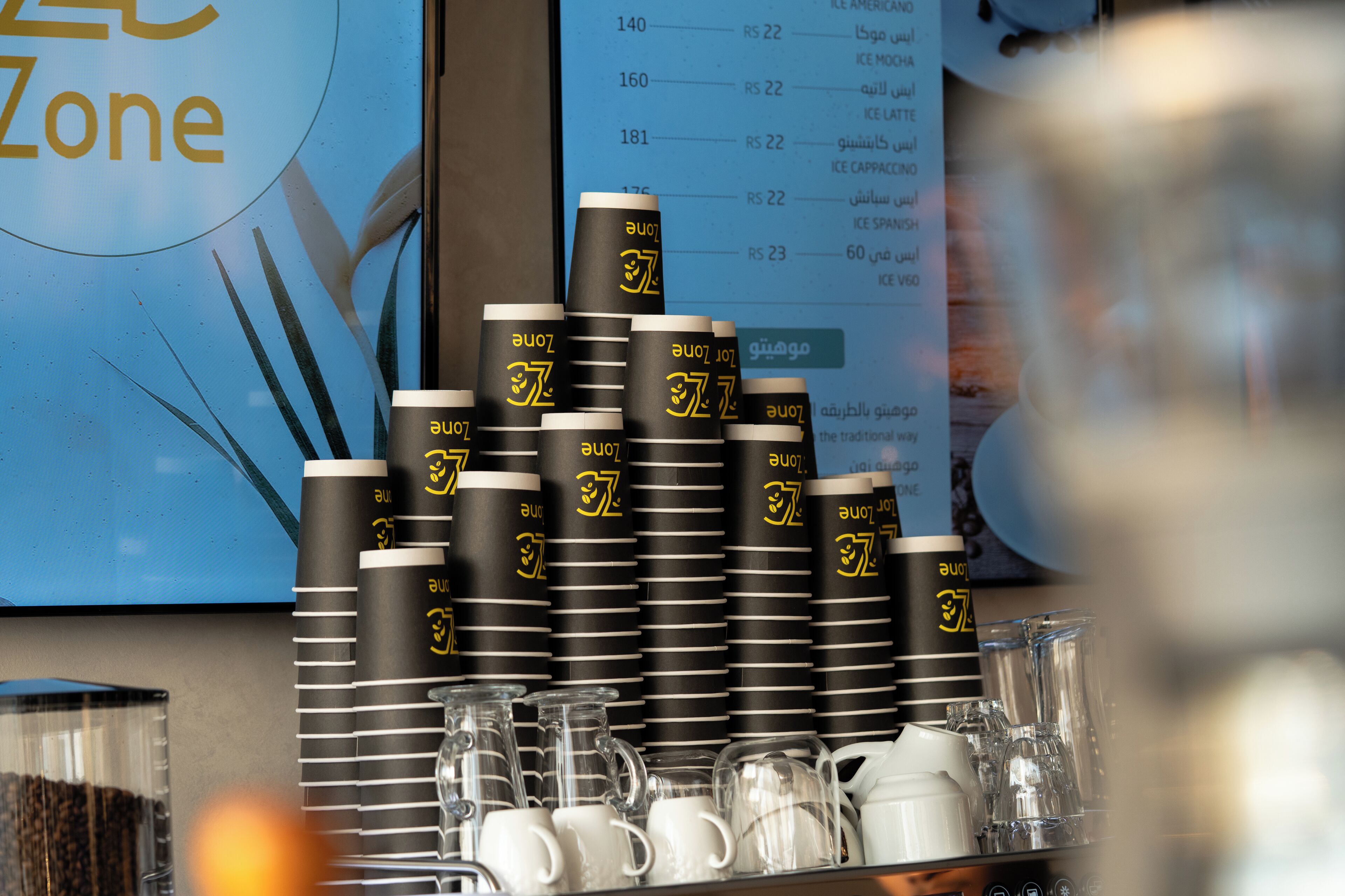 A stack of black and white cups with a logo, a menu board, and a glass container.