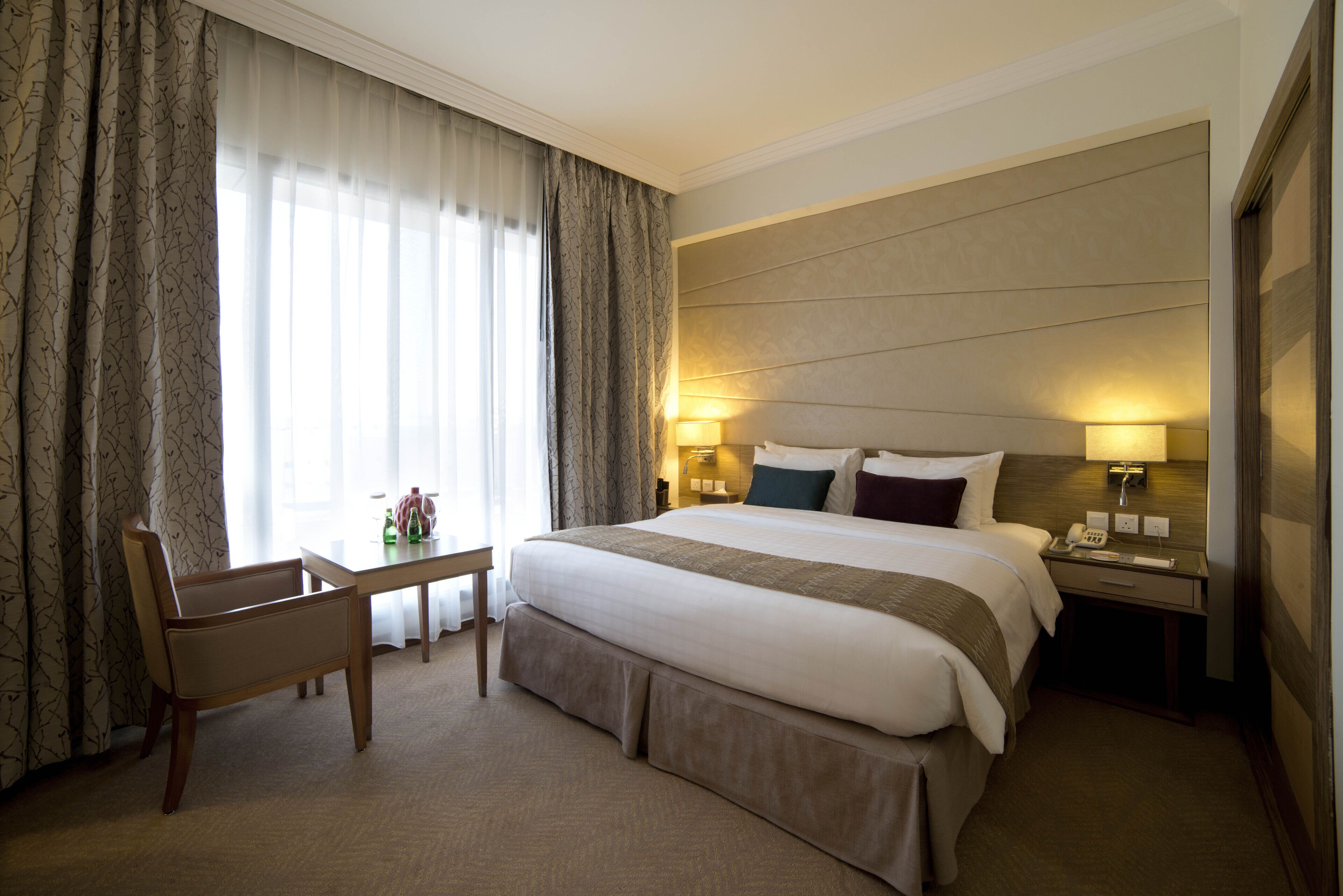 A hotel room with a large bed, a desk, and two bedside lamps.