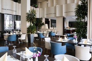 Un restaurant moderne avec des chaises bleues et blanches, des tables en bois foncé et de grandes plantes en pot.