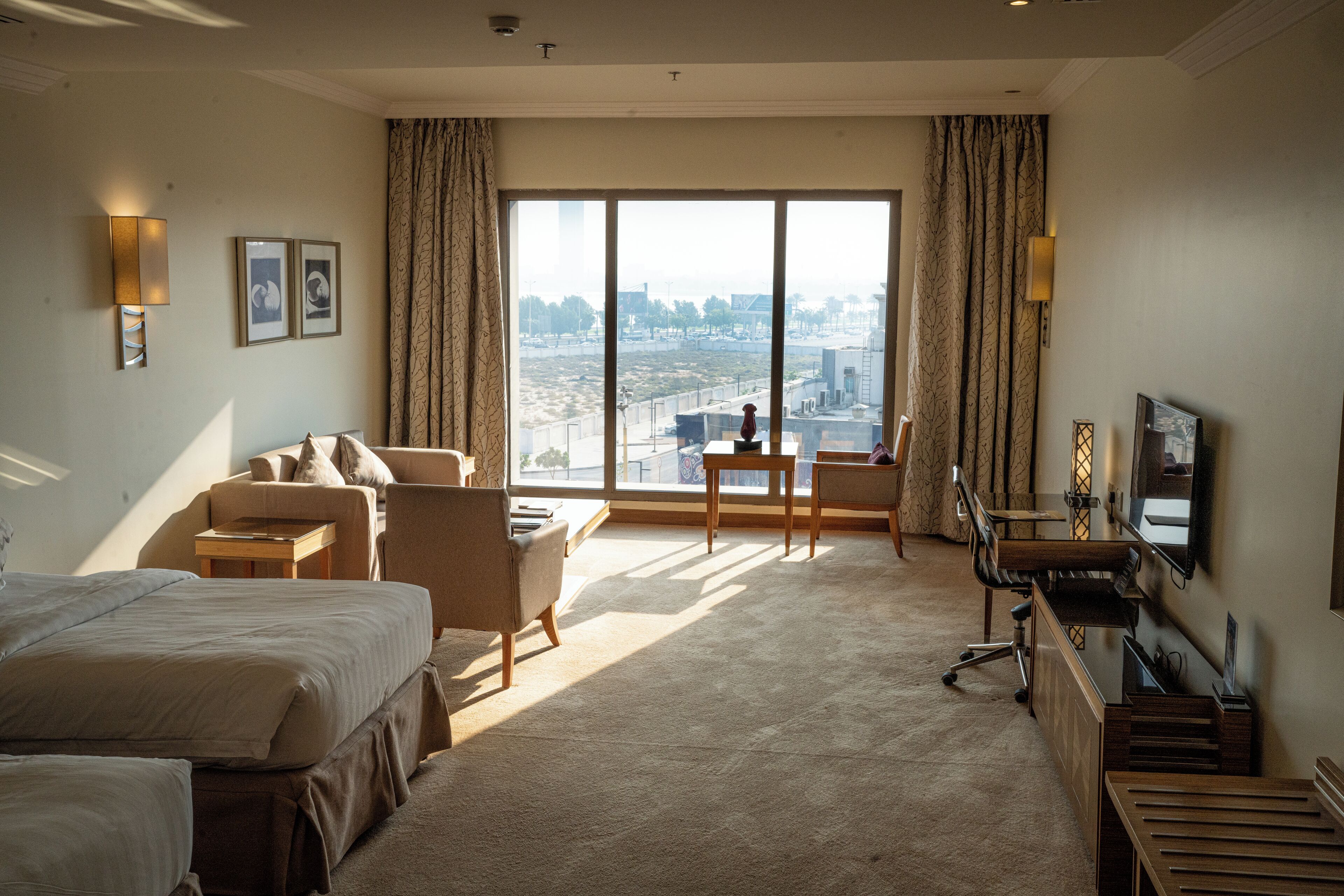 A hotel room with a large window, a bed, a desk, a chair, and a television.