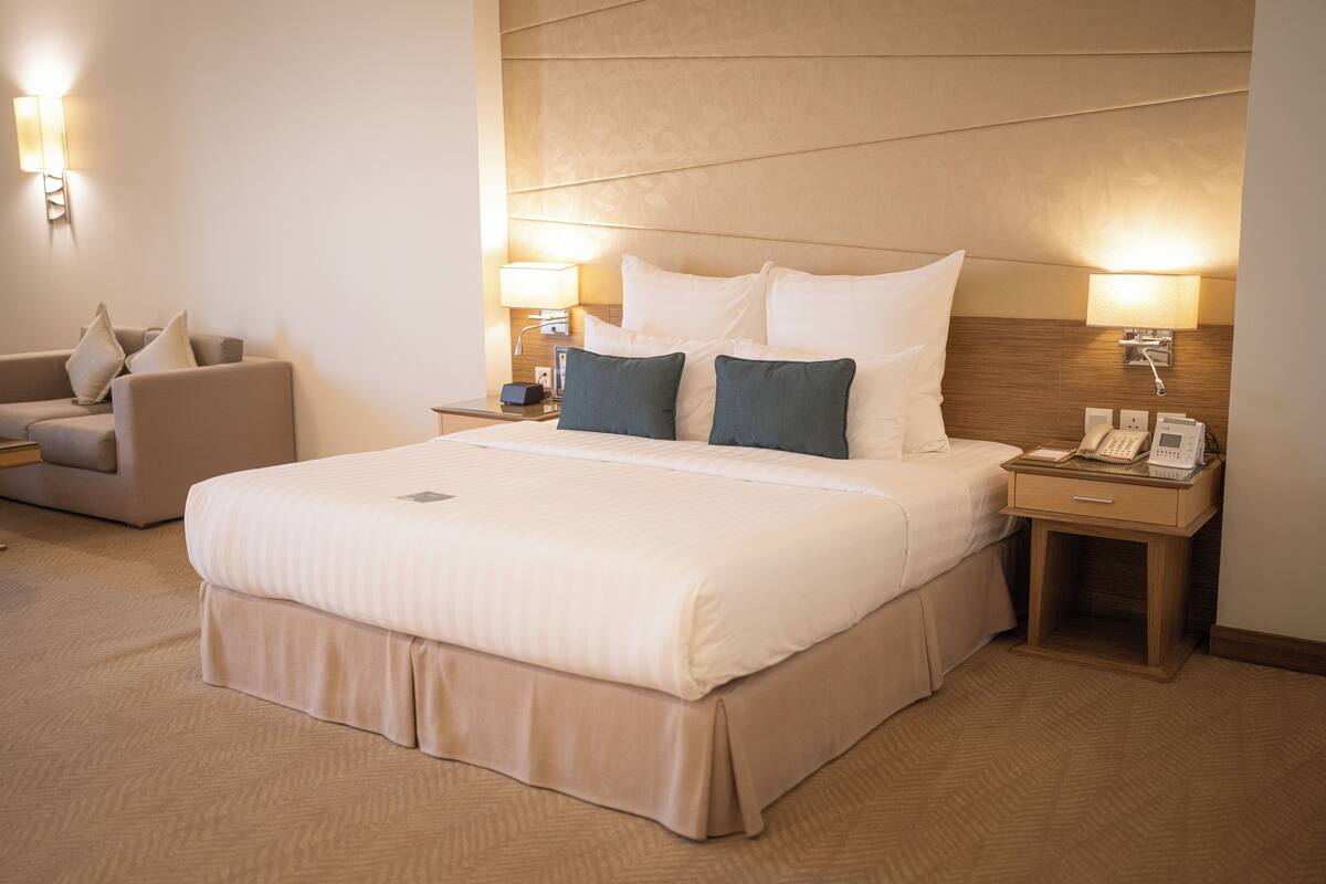 Ein Hotelzimmer mit einem großen Bett, zwei Nachttischen, einer Lampe und einem Sessel.