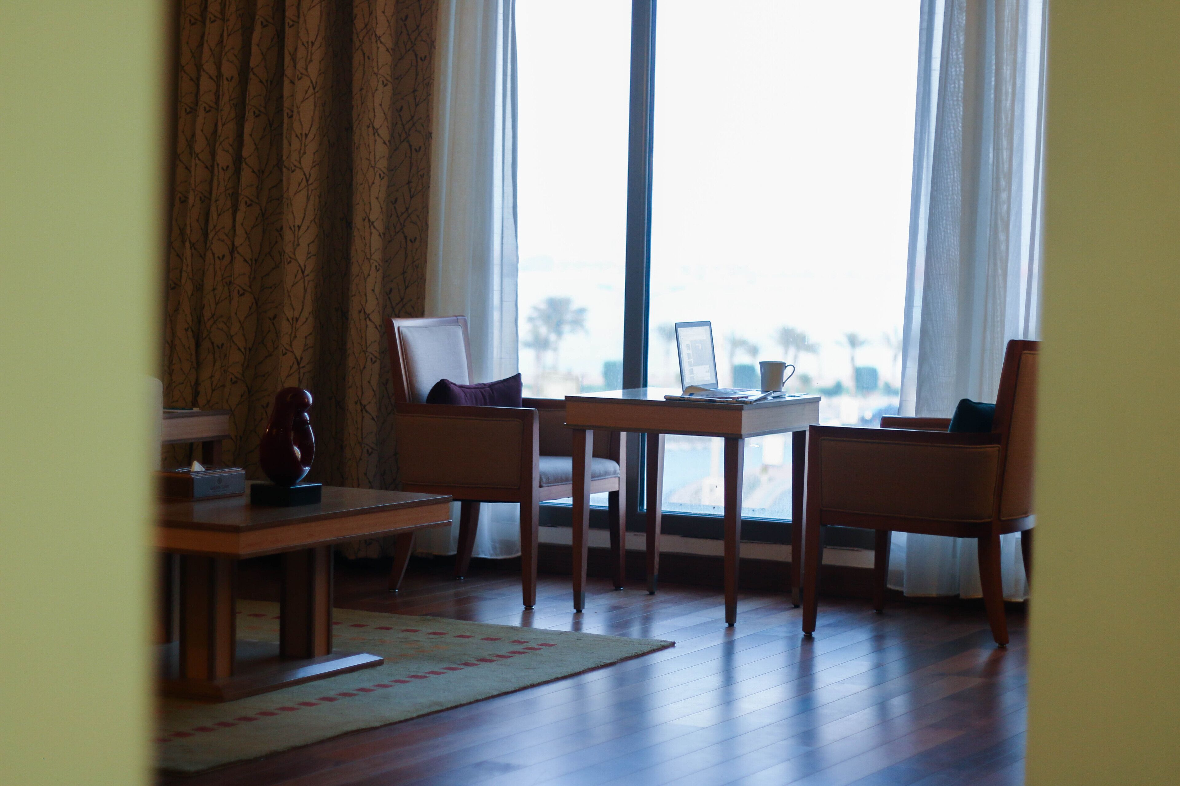 Una habitación con una mesa de madera, dos sillas, una laptop y una ventana con cortinas.