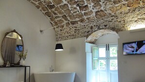 Een badkamer met een stenen plafond, een ruim bad, een spiegel en een televisie aan de muur.
