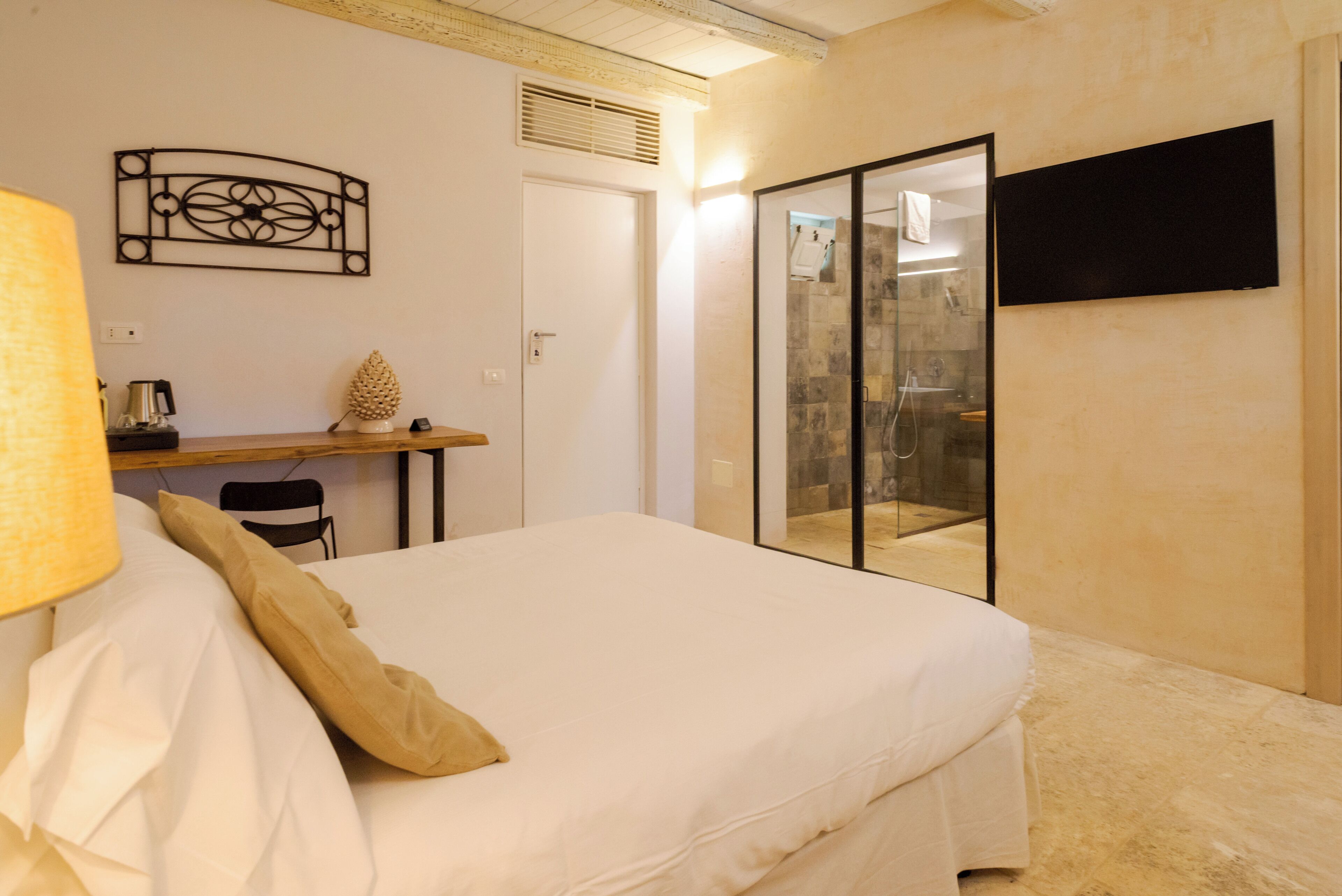 A bedroom with a bed, a desk, a chair, a TV, and a shower area.