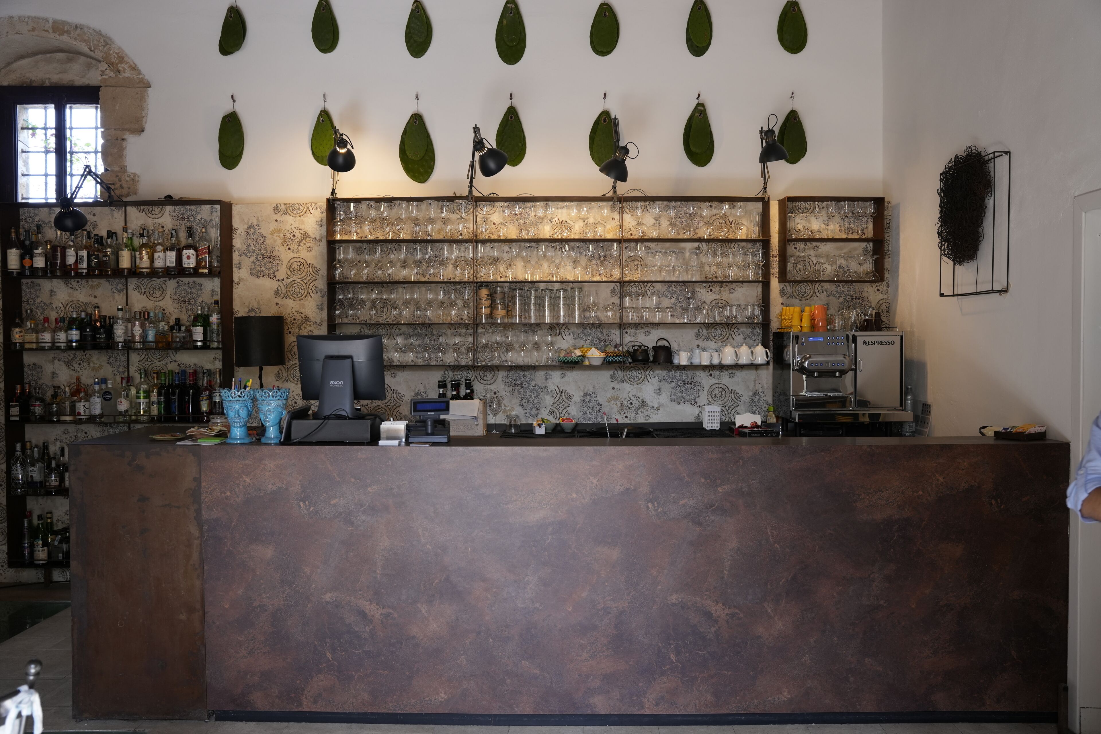 Een bar met een toog, planken vol flessen en een koffieapparaat.