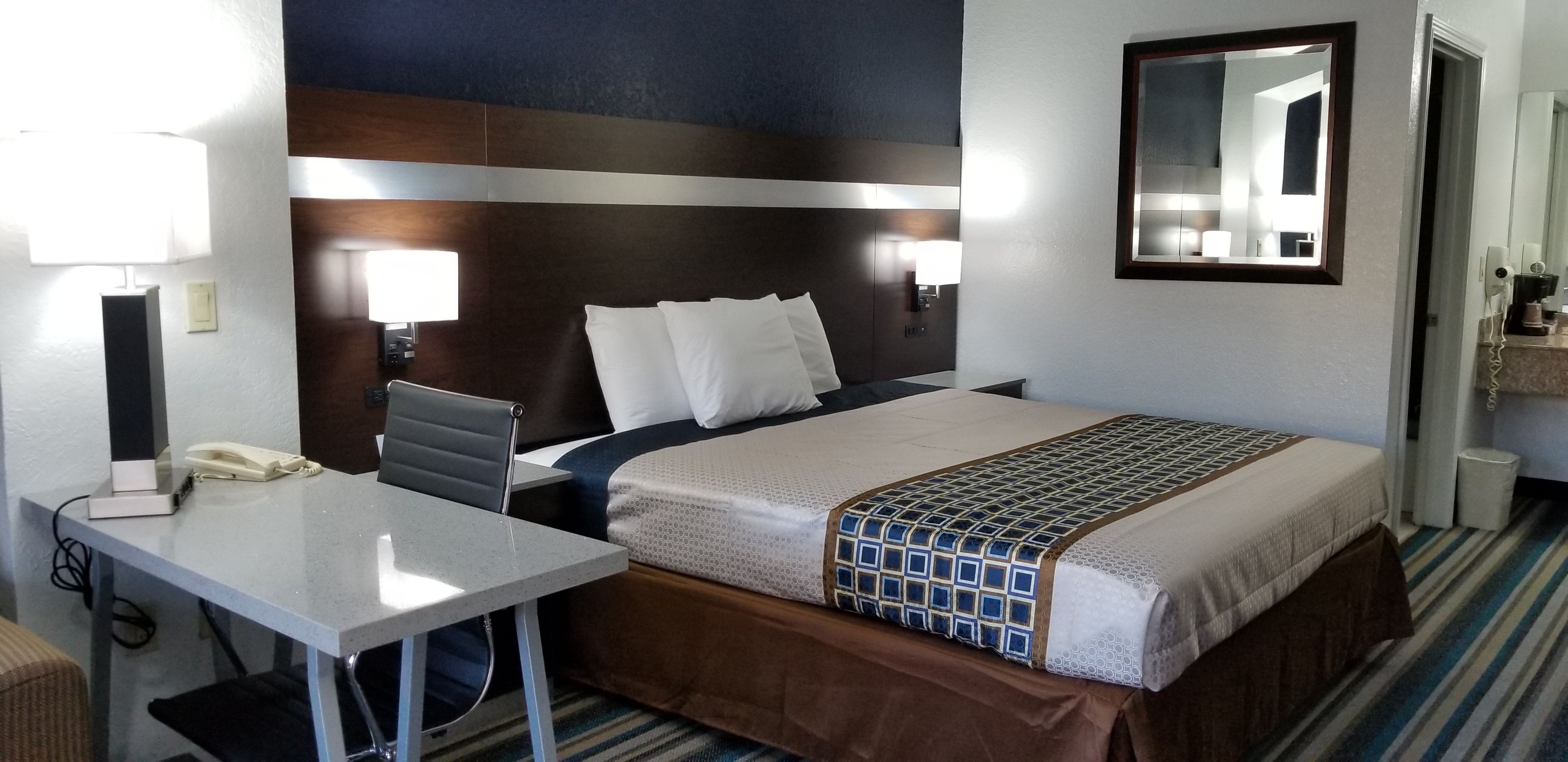 A hotel room with a bed, bedside lamps, a desk with a phone, and a mirror on the wall.