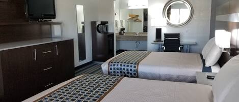 A hotel room with two beds, a TV, a mirror, a desk, and a bathroom.