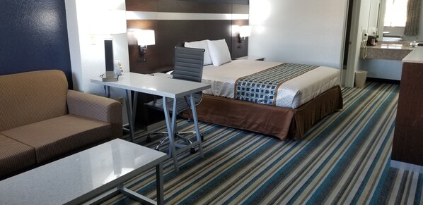 A hotel room with a bed, a desk, a chair, a sofa, and a bathroom.