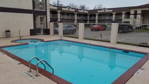 A rectangular swimming pool with a 3 ft depth marker, surrounded by a fence and a building with balconies.
