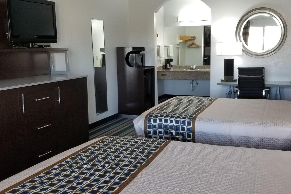 A hotel room with two beds, a TV, a coffee machine, a mirror, and a small desk with a lamp.