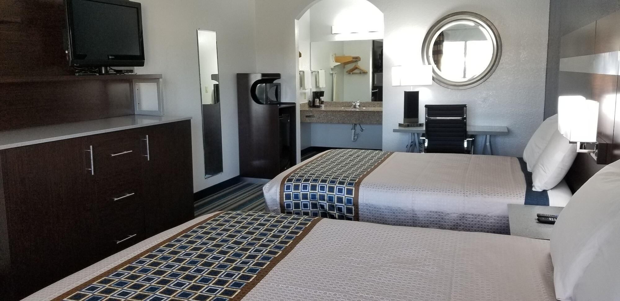 Une chambre d’hôtel avec deux lits, une télévision, une machine à café, un miroir et un petit bureau avec une lampe.