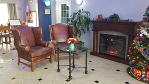 A hotel lobby with leather armchairs, a glass table, a fireplace, a Christmas tree, and a sign indicating a no smoking area. - HomeBridge Inn and Suites (Beaumont)