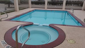 A rectangular swimming pool with a surrounding brick deck and a separate circular hot tub area. - HomeBridge Inn and Suites (Beaumont)