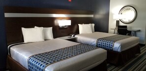 A hotel room with two beds, a nightstand, a lamp, and a mirror.