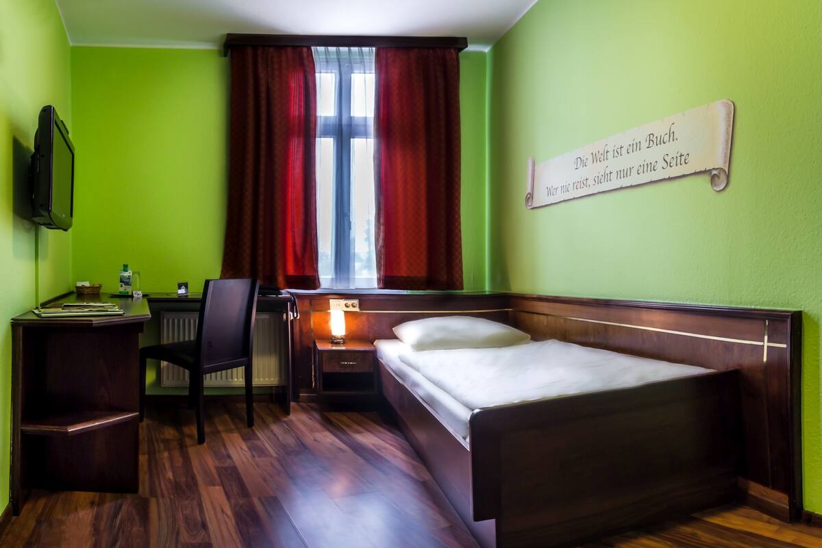A hotel room with a bed, desk, chair, and a wall-mounted TV.