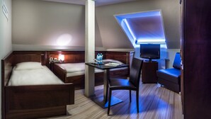 Habitación de hotel compacta con dos camas, un escritorio con silla, un televisor y una pequeña zona de estar.