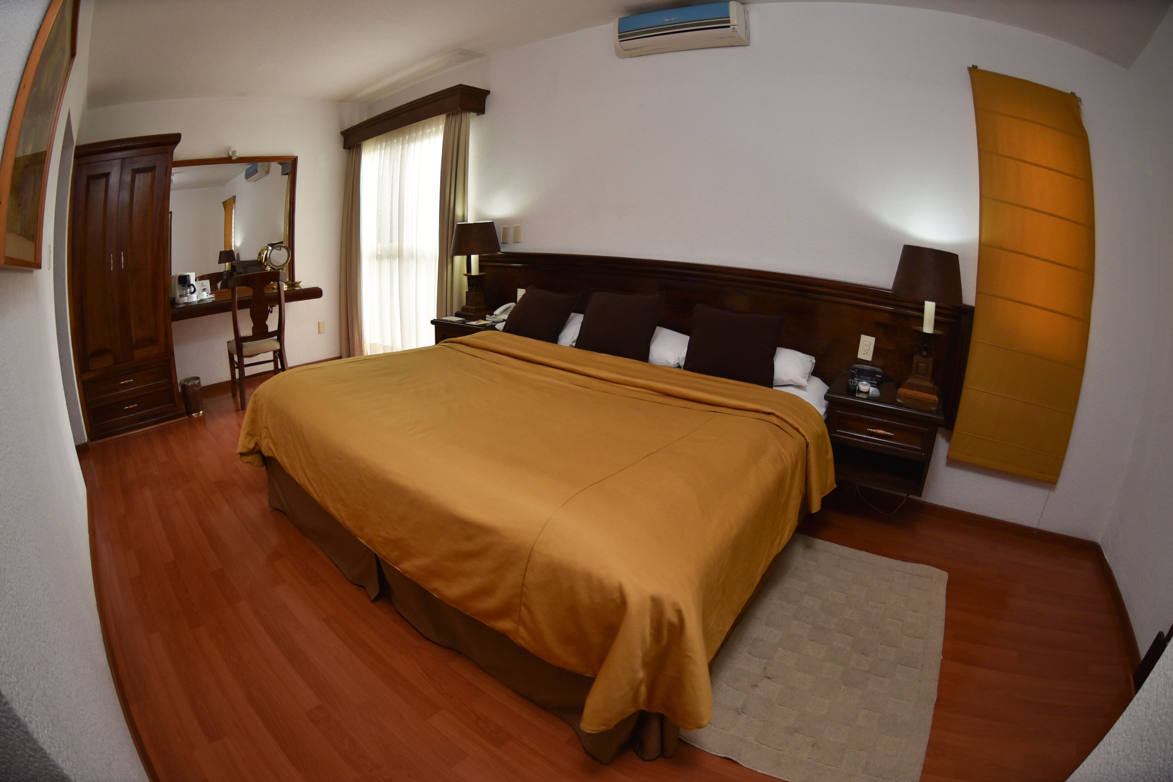 Une chambre d’hôtel avec un grand lit, des meubles en bois, un bureau avec une chaise, une table de chevet et un miroir.