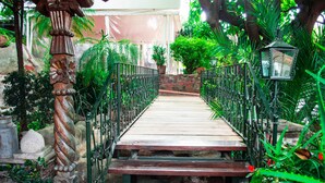 Una escalera de madera con barandales de metal que lleva a un espacio cubierto con plantas y un muro de piedra.