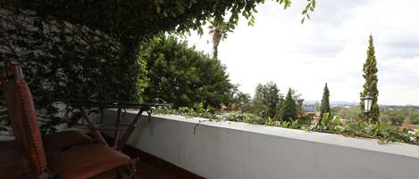 A terrace with a white wall, a wooden chair, and a metal ladder.