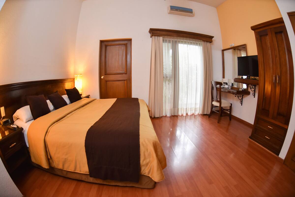 Une chambre d’hôtel avec un grand lit, un bureau avec une chaise, une télévision et une armoire.