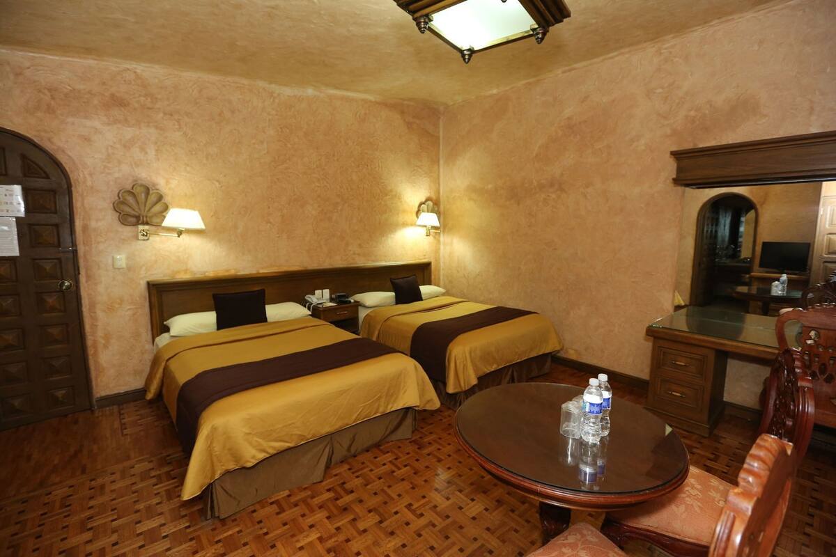 Une chambre d’hôtel avec deux lits, un plancher en bois, une table ronde avec des bouteilles d’eau et un miroir.