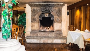Una chimenea de piedra con fuego, rodeada de sillas de madera y una mesa lista para comer.