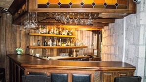 Zona de bar con estantes de madera llenos de botellas, copas colgando y taburetes acolchados.