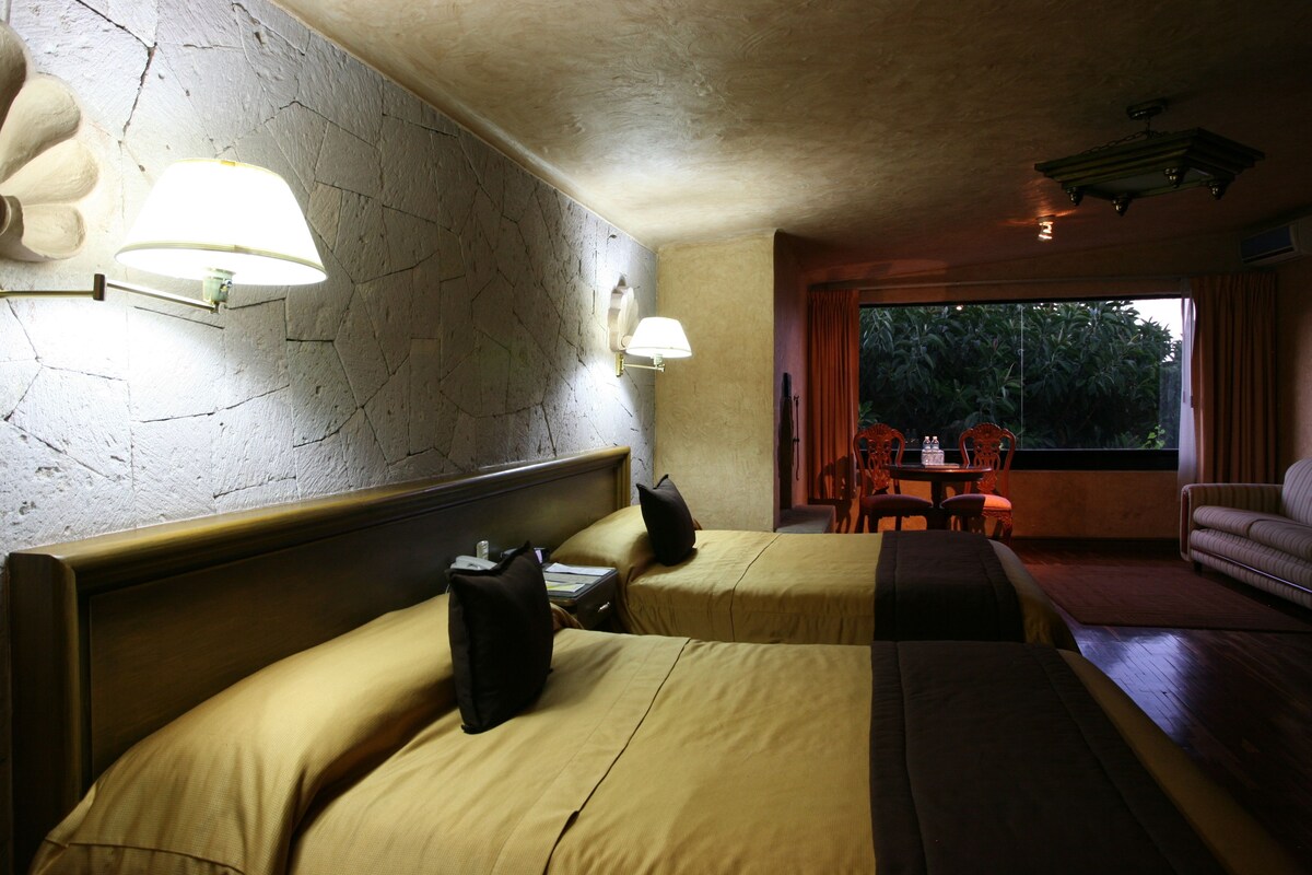 Habitación de hotel con dos camas, un sofá, una mesa de comedor y vistas al exterior.