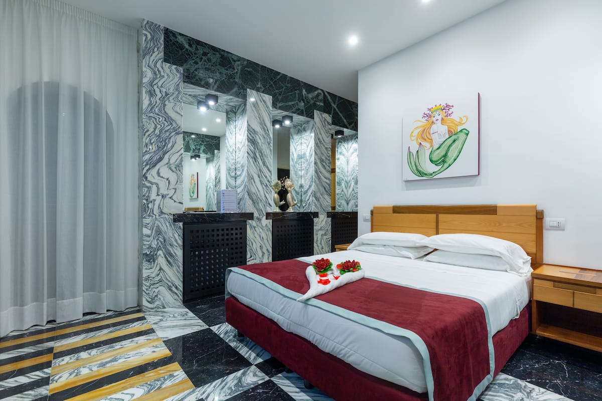 A hotel room with a bed, a nightstand, a mirror, and a marble-patterned wall.