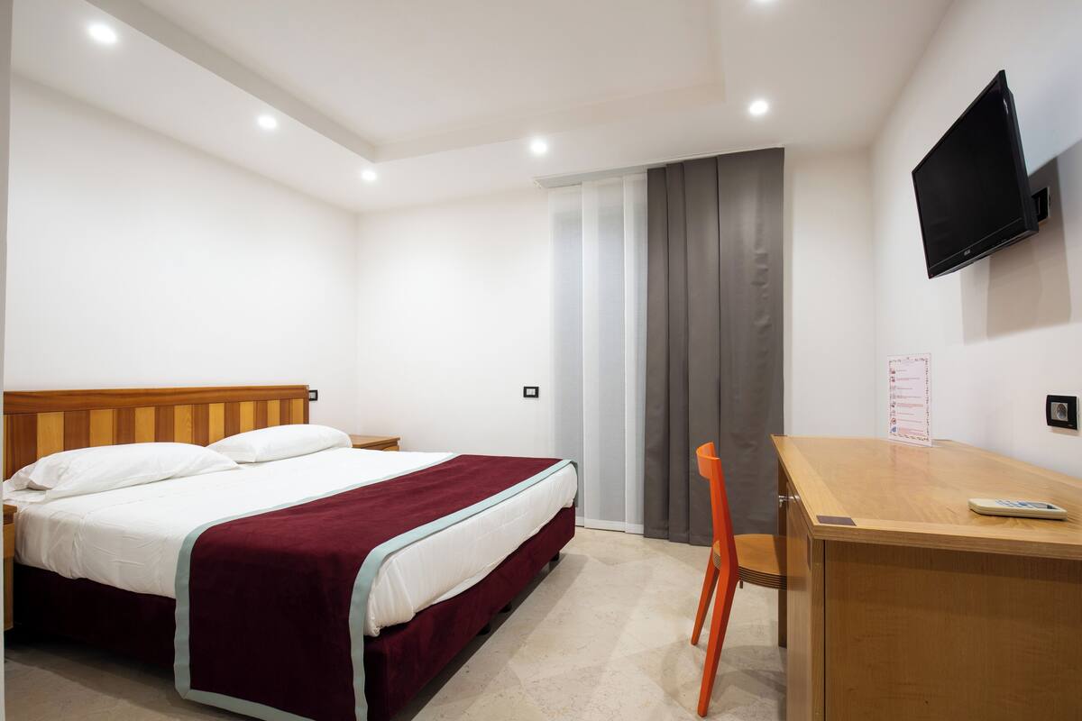 A bedroom with a bed, a desk, a chair, a TV, and a wardrobe.