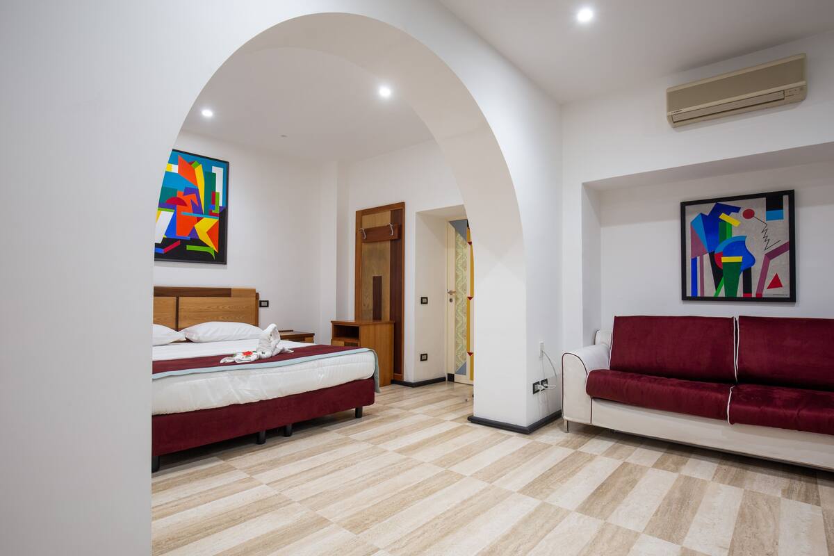 A modern hotel room with a bed, a red sofa, and two abstract paintings.