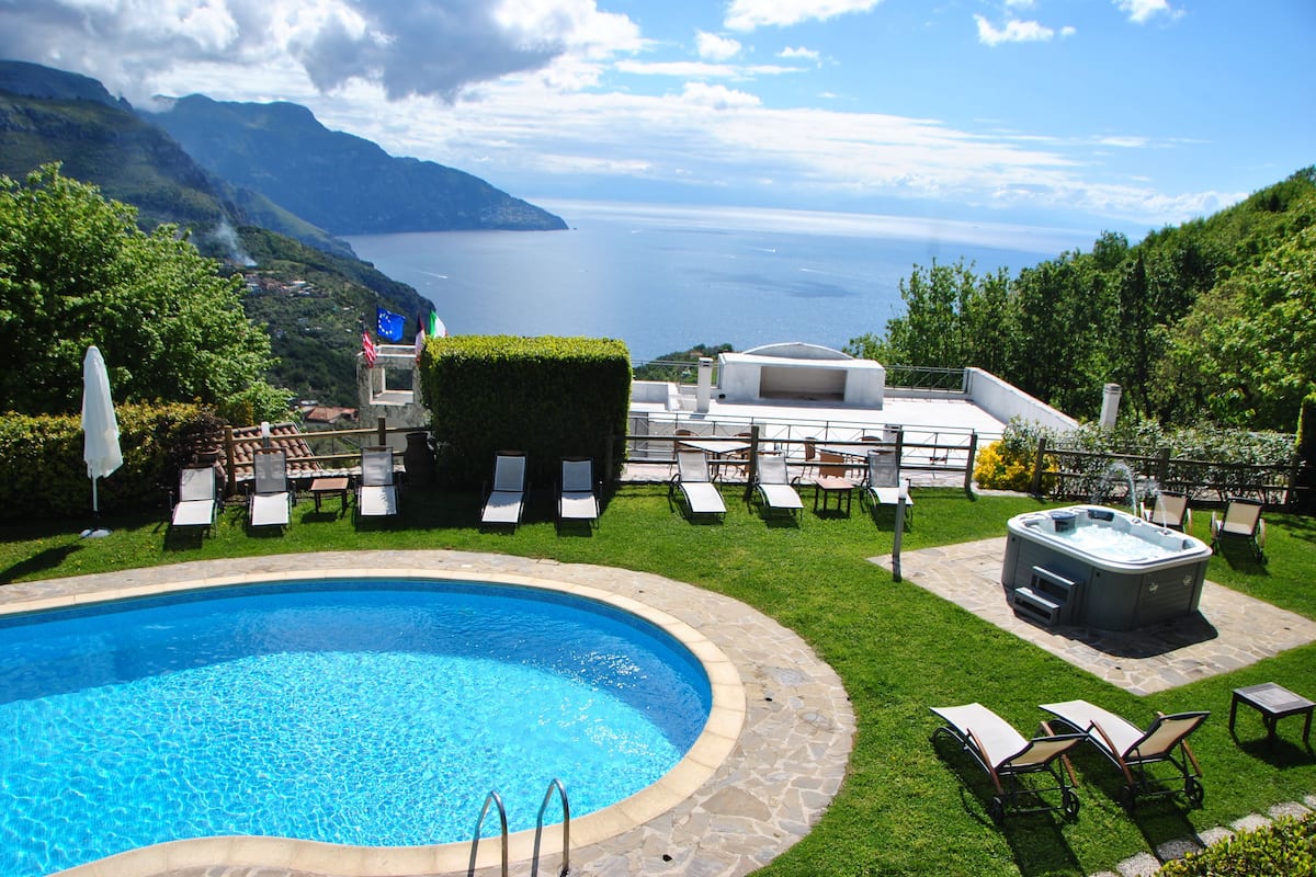 A pool area with a hot tub, lounge chairs, and a view of the sea.