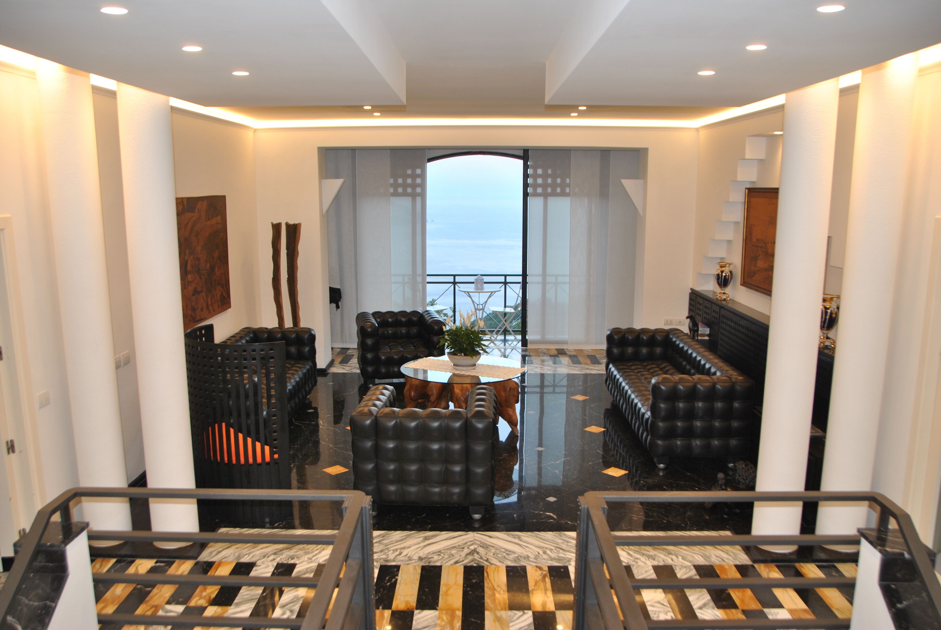 A spacious lobby with a high ceiling, a central seating area with sofas and a coffee table, and a view of the sea through a large window.