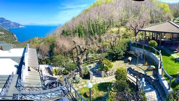 Un jardín con un pabellón, senderos de piedra y vistas al mar.