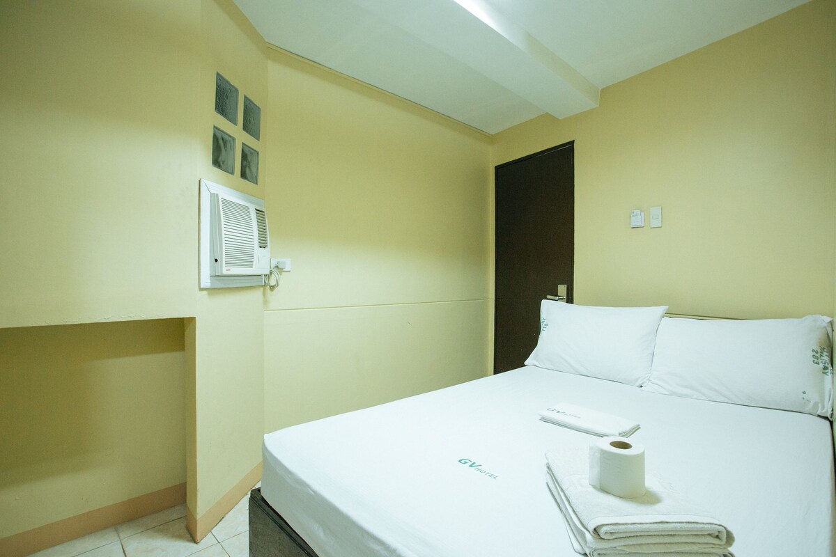 A hotel room with a bed, a wall-mounted air conditioner, a door, and a towel on the bed.