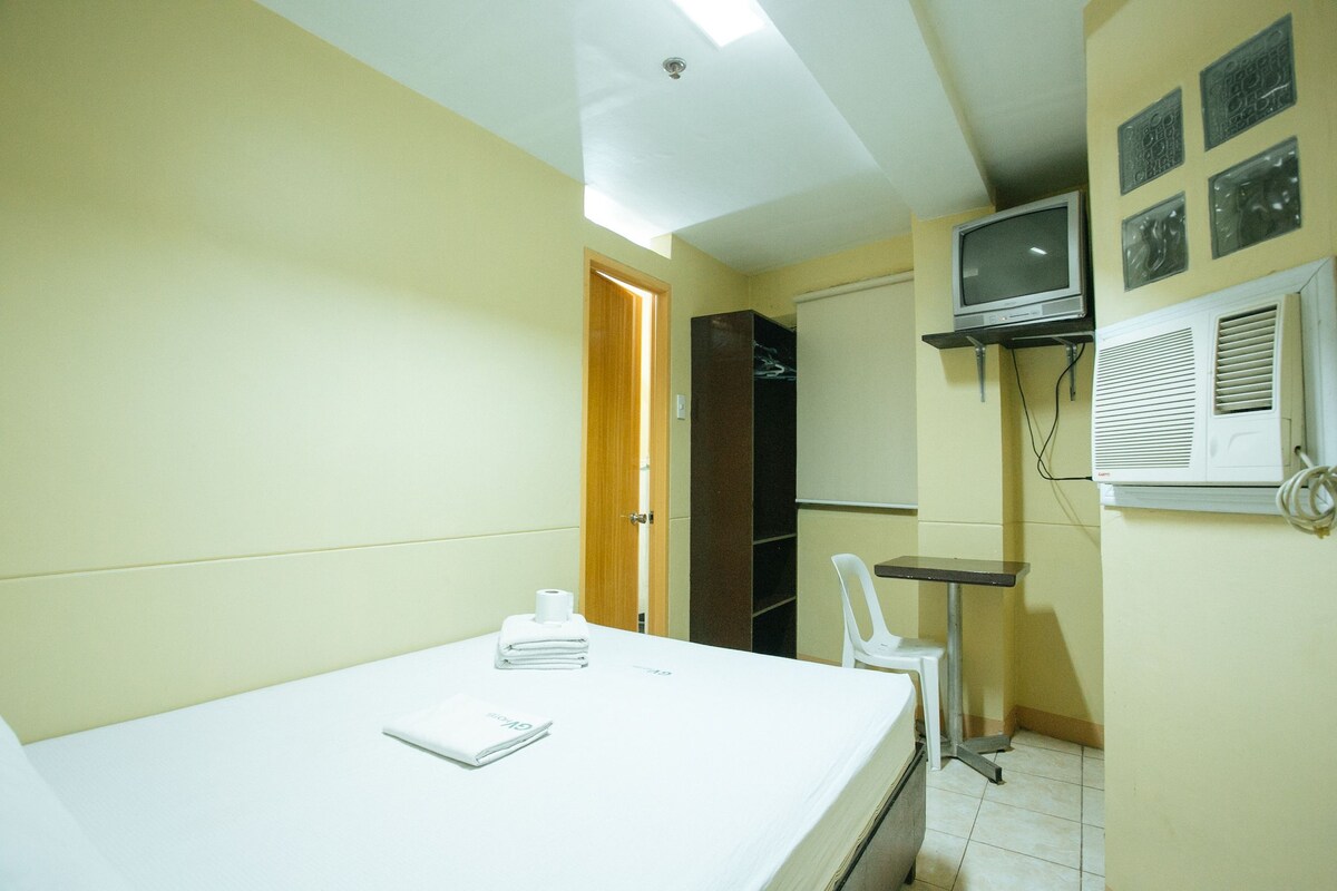 A small hotel room with a bed, a chair, a TV, and a wardrobe.