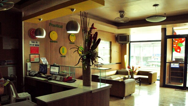 A reception area with a counter, a plant, a clock, and a sign indicating a shower. - GV Hotels Talisay City (Talisay)