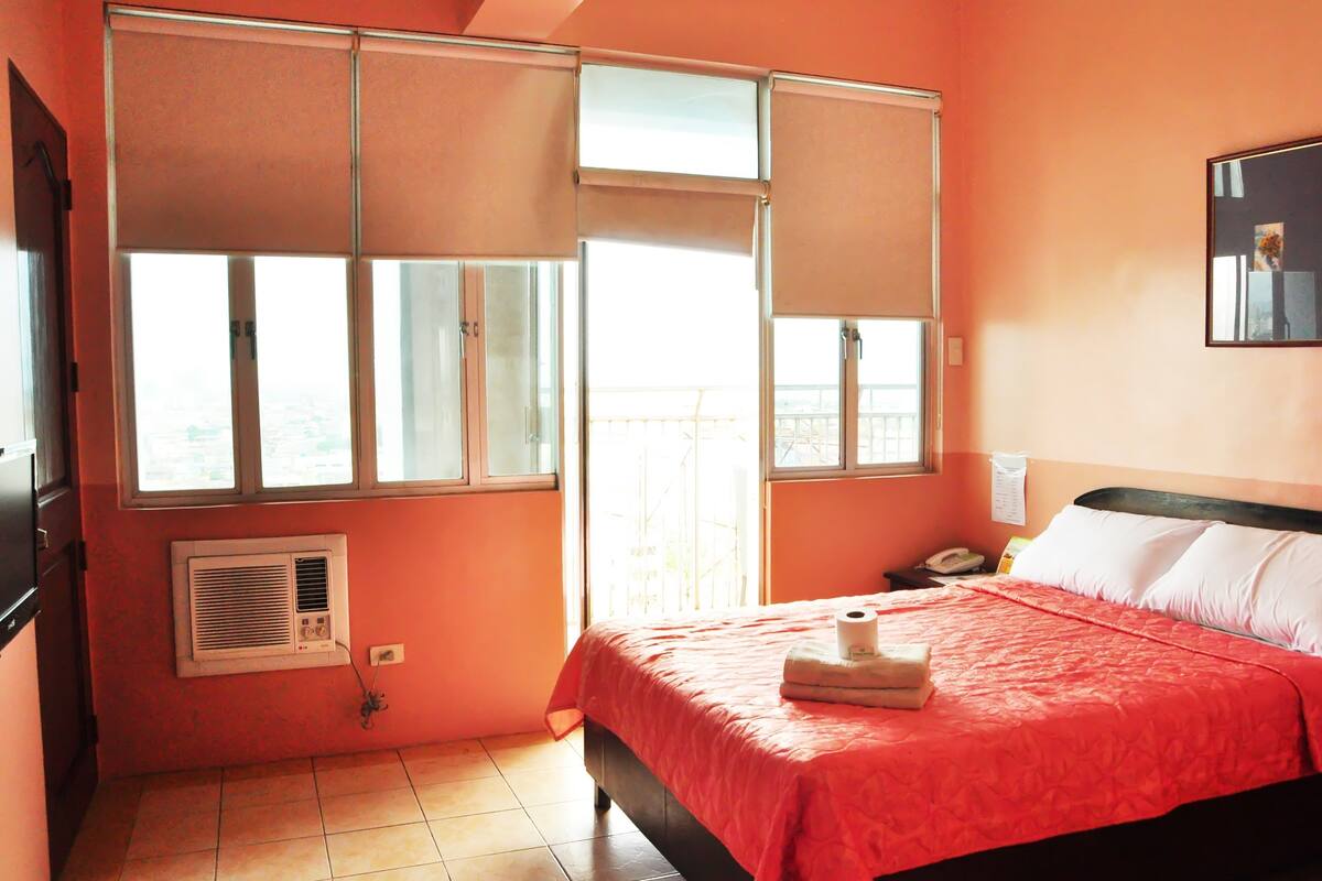 A bedroom with a bed, a window, a radiator, and a wall-mounted telephone.